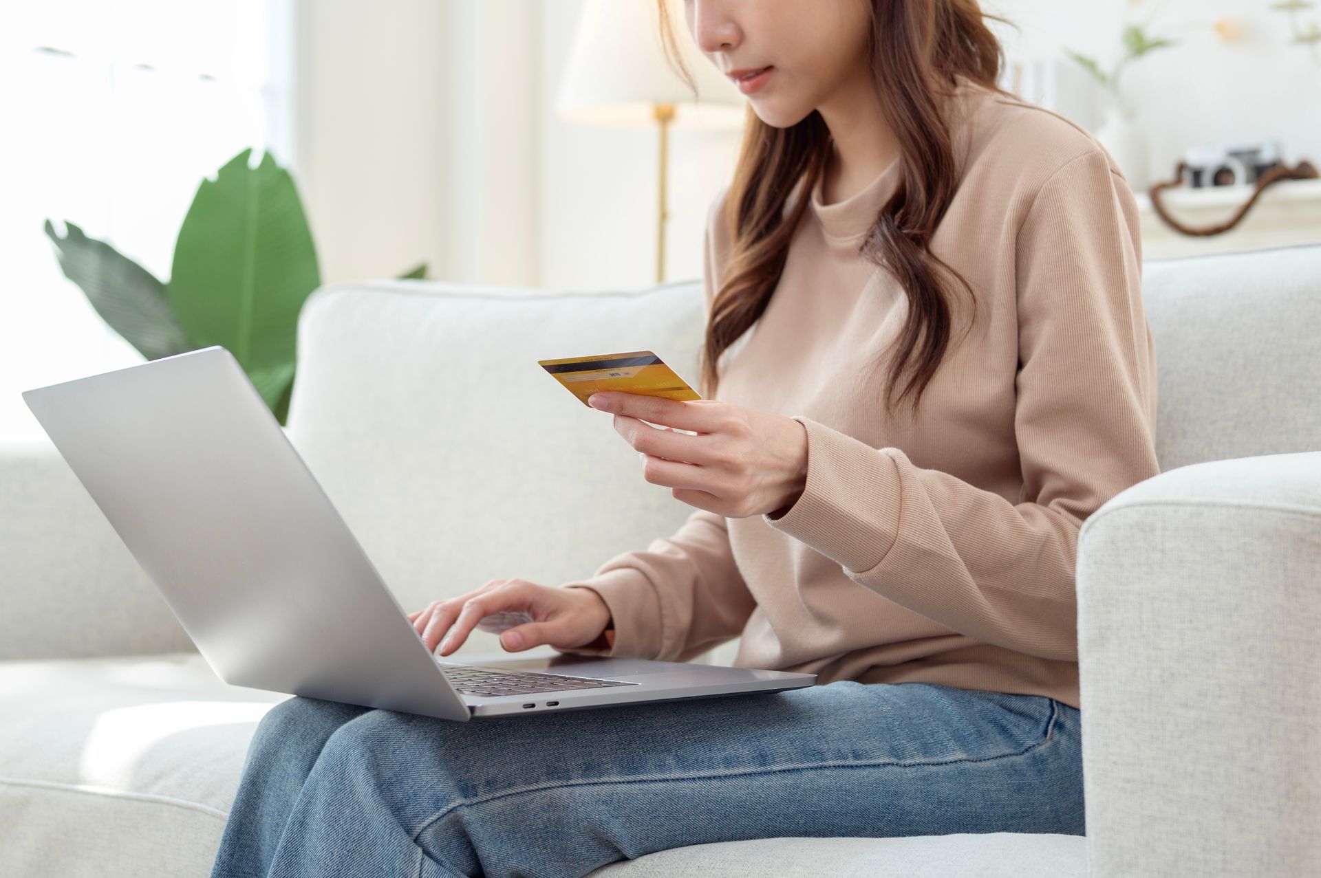 Woman on a couch using a laptop and credit card for online shopping.