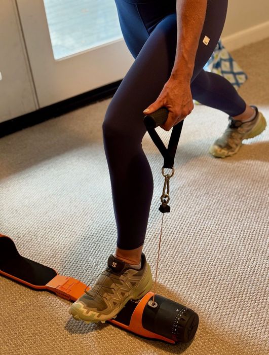Person in blue leggings exercising with a cable machine, indoors. Focus on the leg and foot.