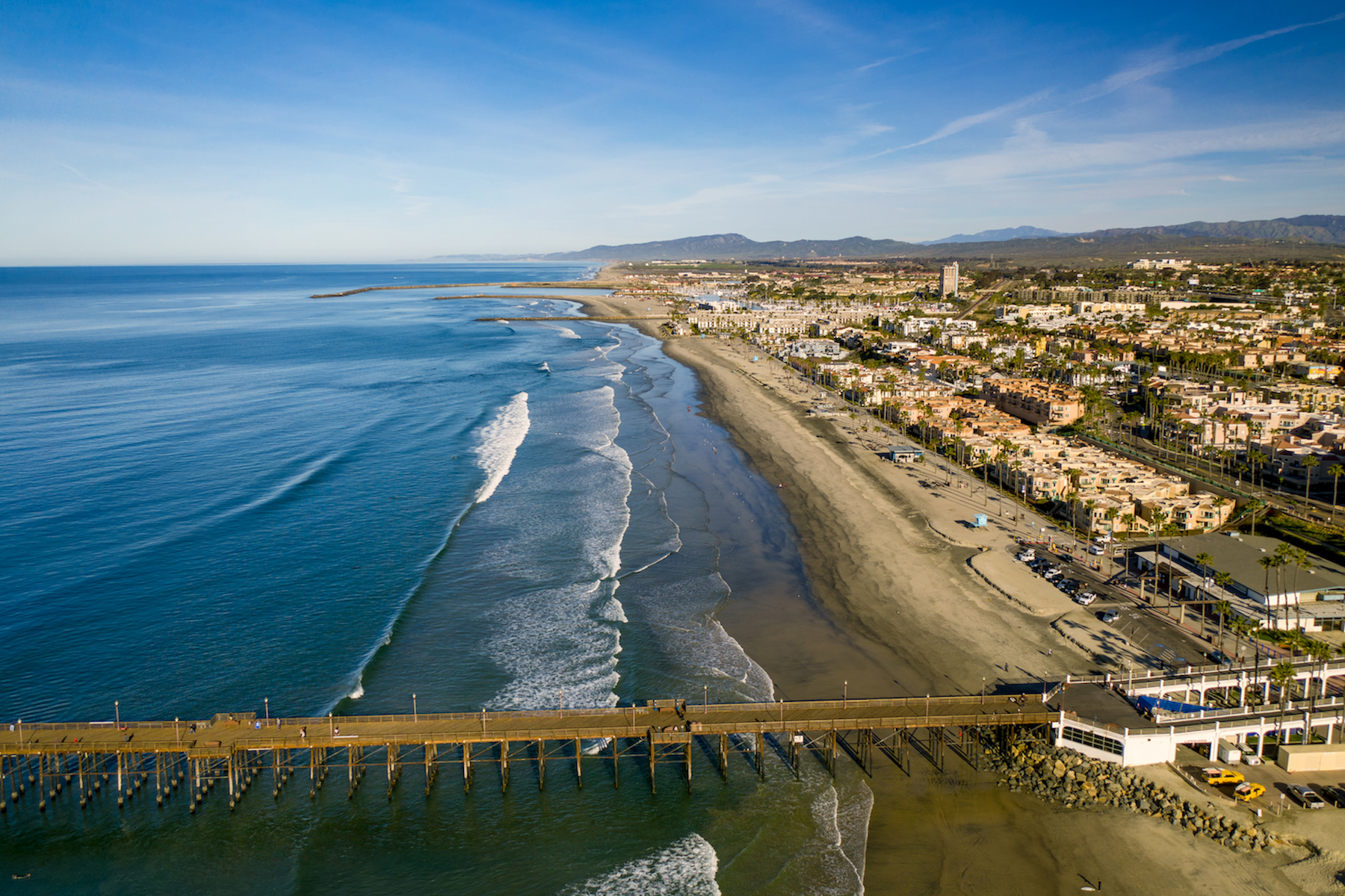 Aerial view of a sandy beach and ocean shoreline beside a coastal town and pier