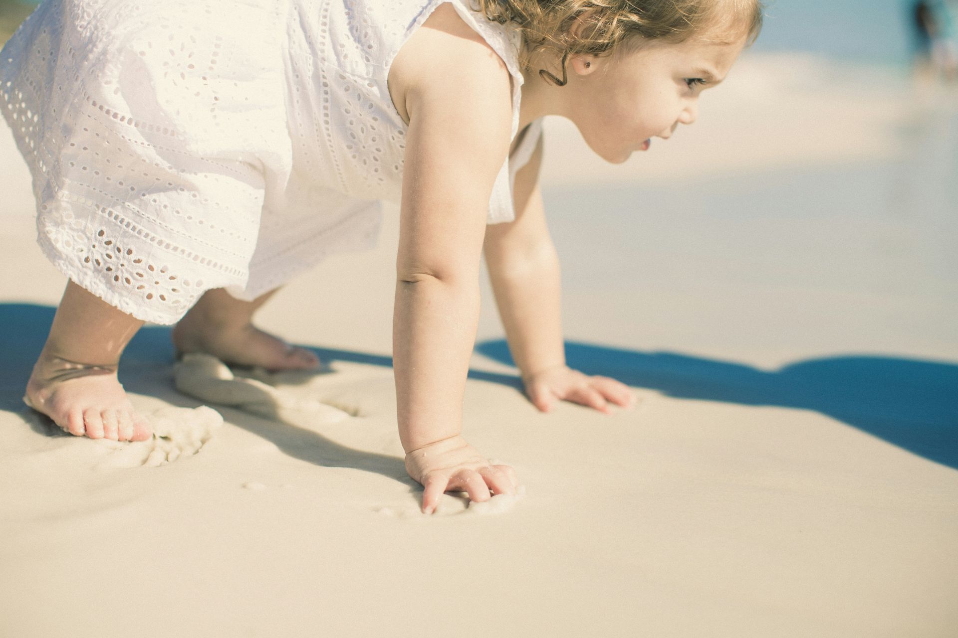 Girl in white dress crawling on sandy beach.