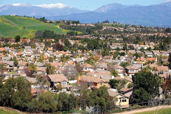 Suburban neighborhood with houses among green hills, with mountains in the background under a clear sky
