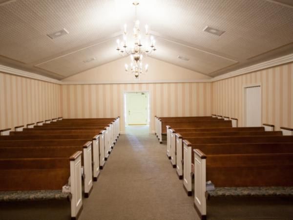 A church with rows of wooden benches and a chandelier hanging from the ceiling.