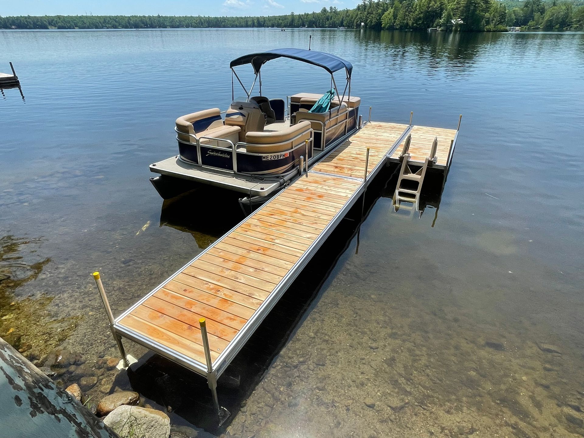 A pontoon boat is docked at a wooden dock on a lake.