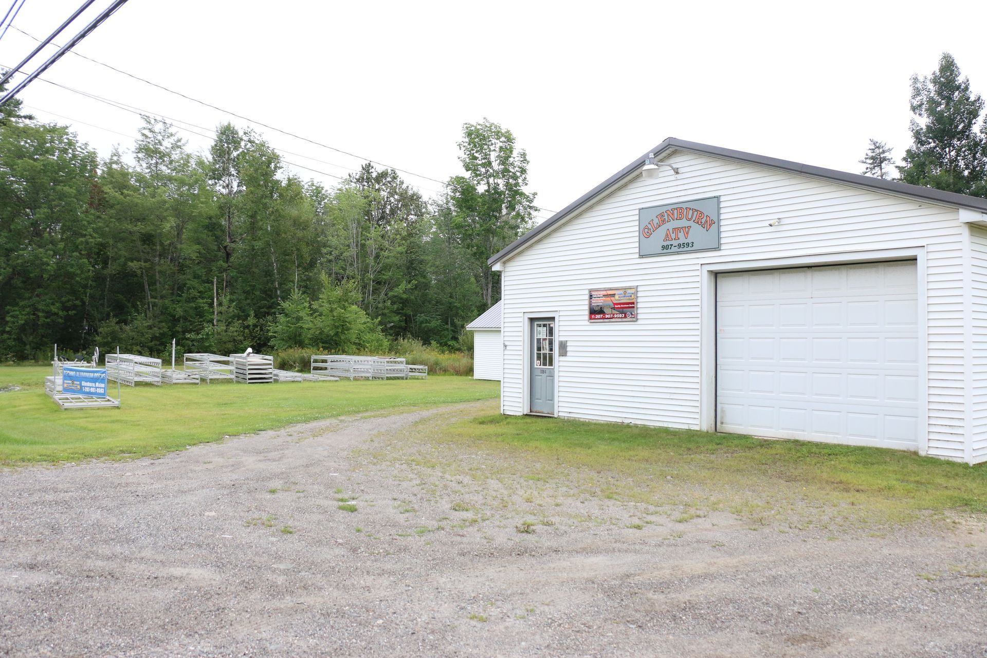 A white building with a garage door is sitting in the middle of a grassy field.