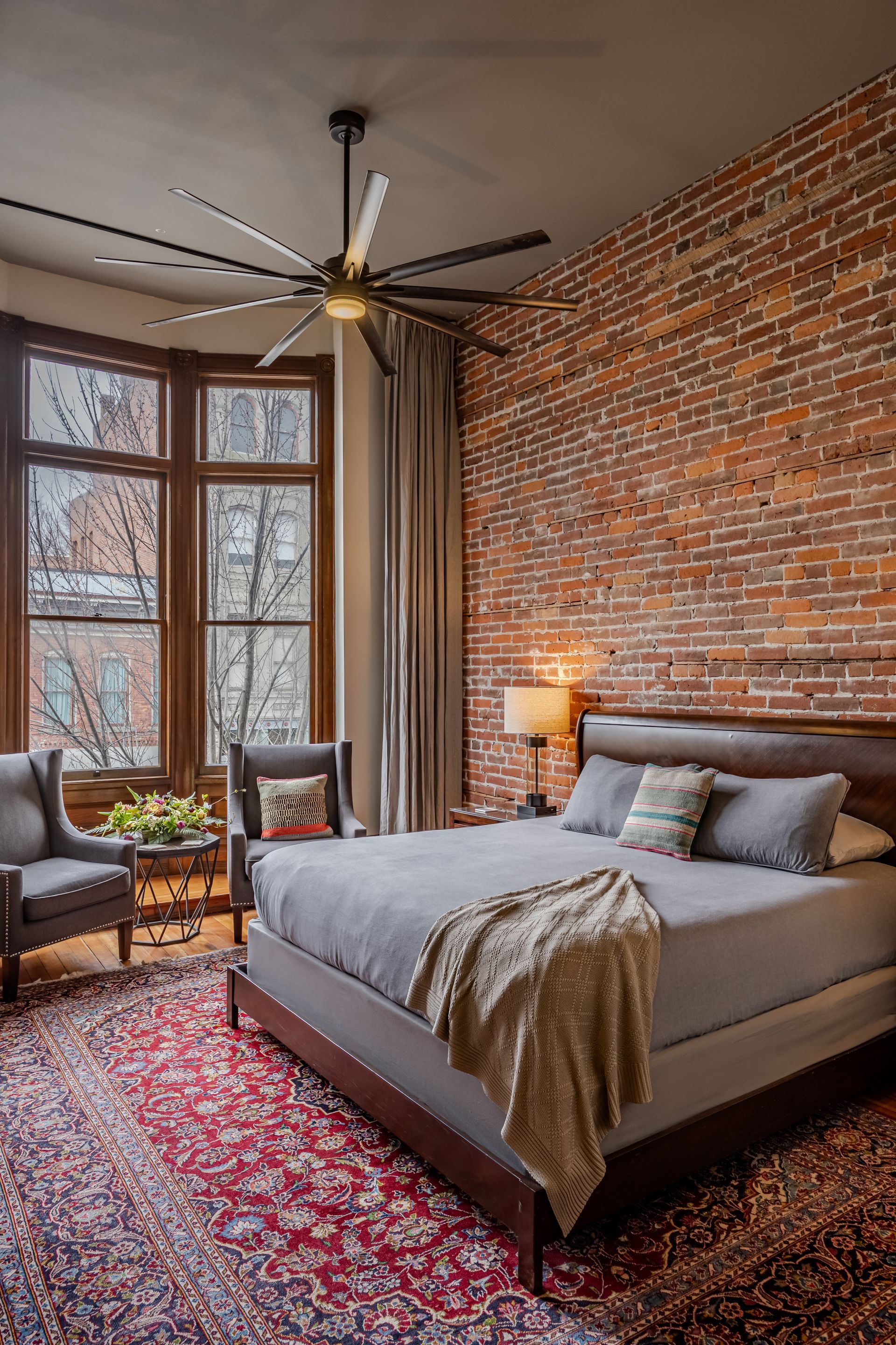 A bedroom with a bed , chairs , a rug and a ceiling fan.