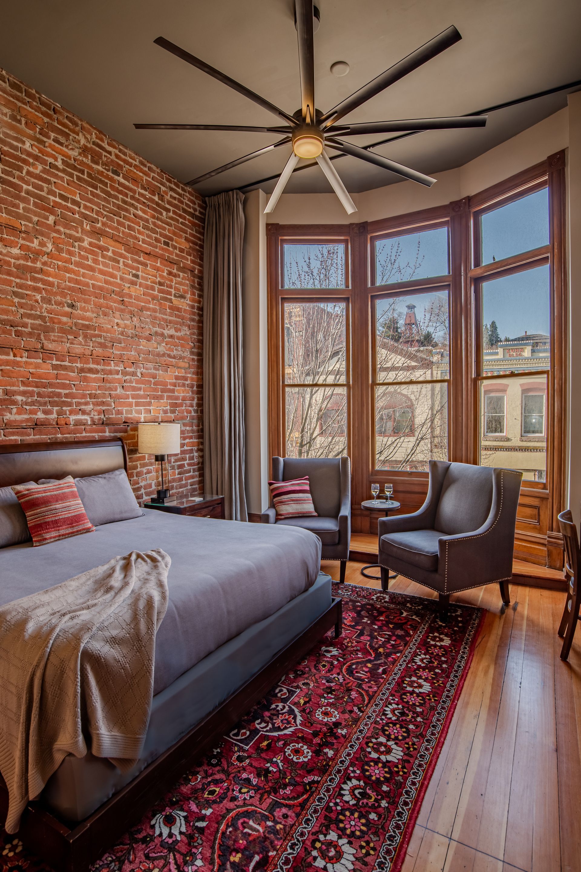 A bedroom with a bed , chairs , a rug and a ceiling fan.
