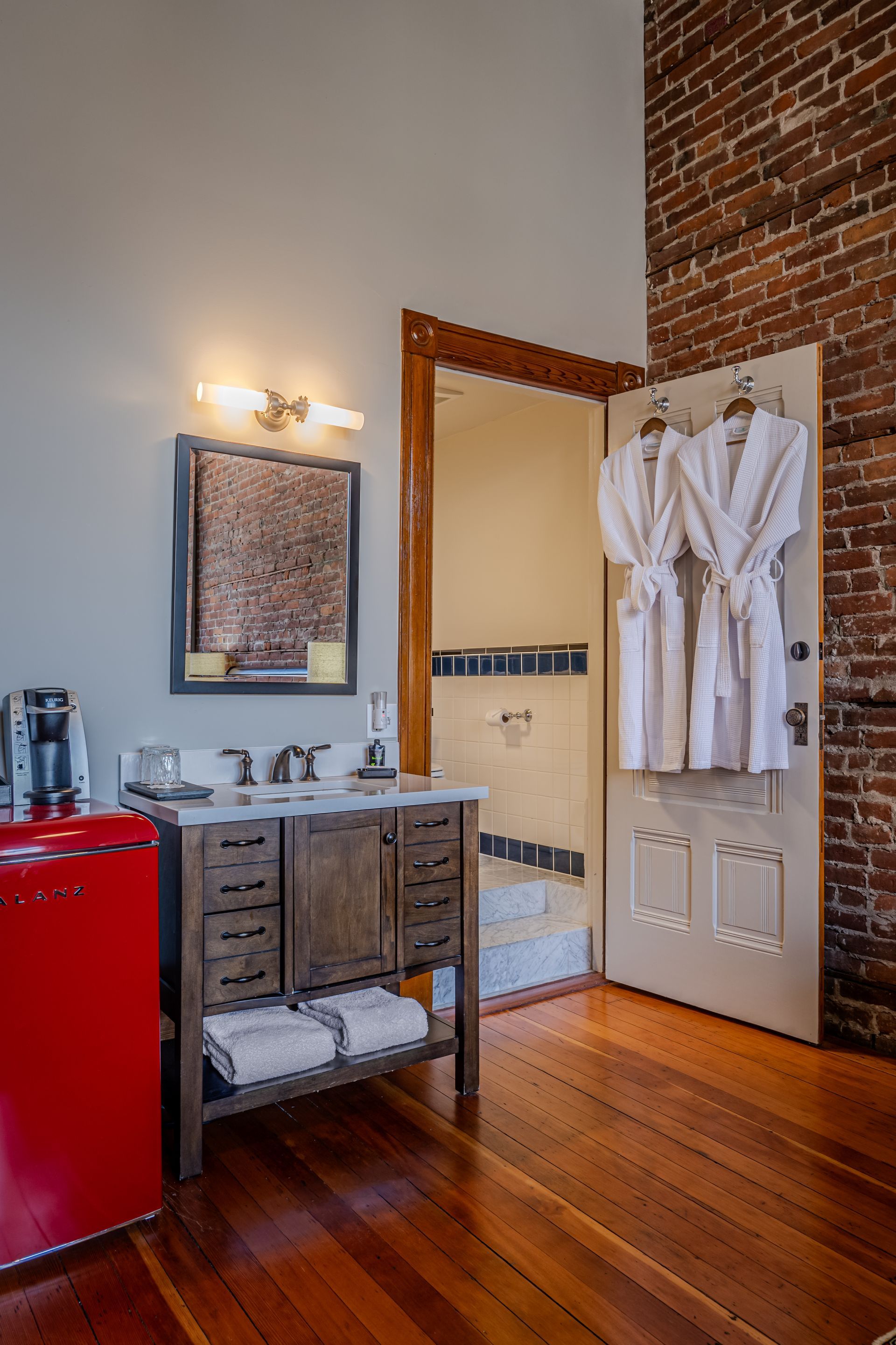 A bathroom with two bathrobes hanging on the door and a red refrigerator.