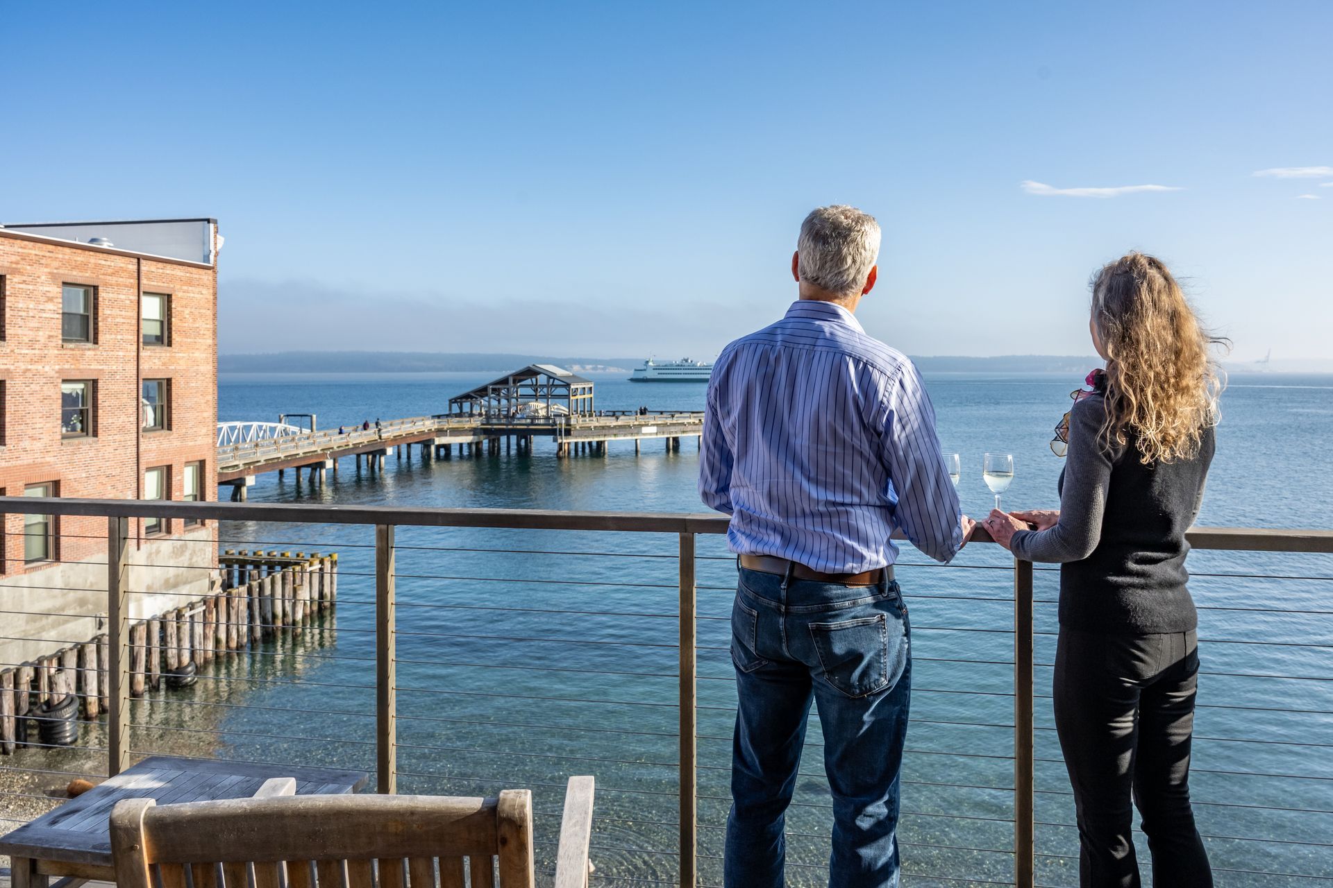A man and a woman are standing on a balcony overlooking the ocean.