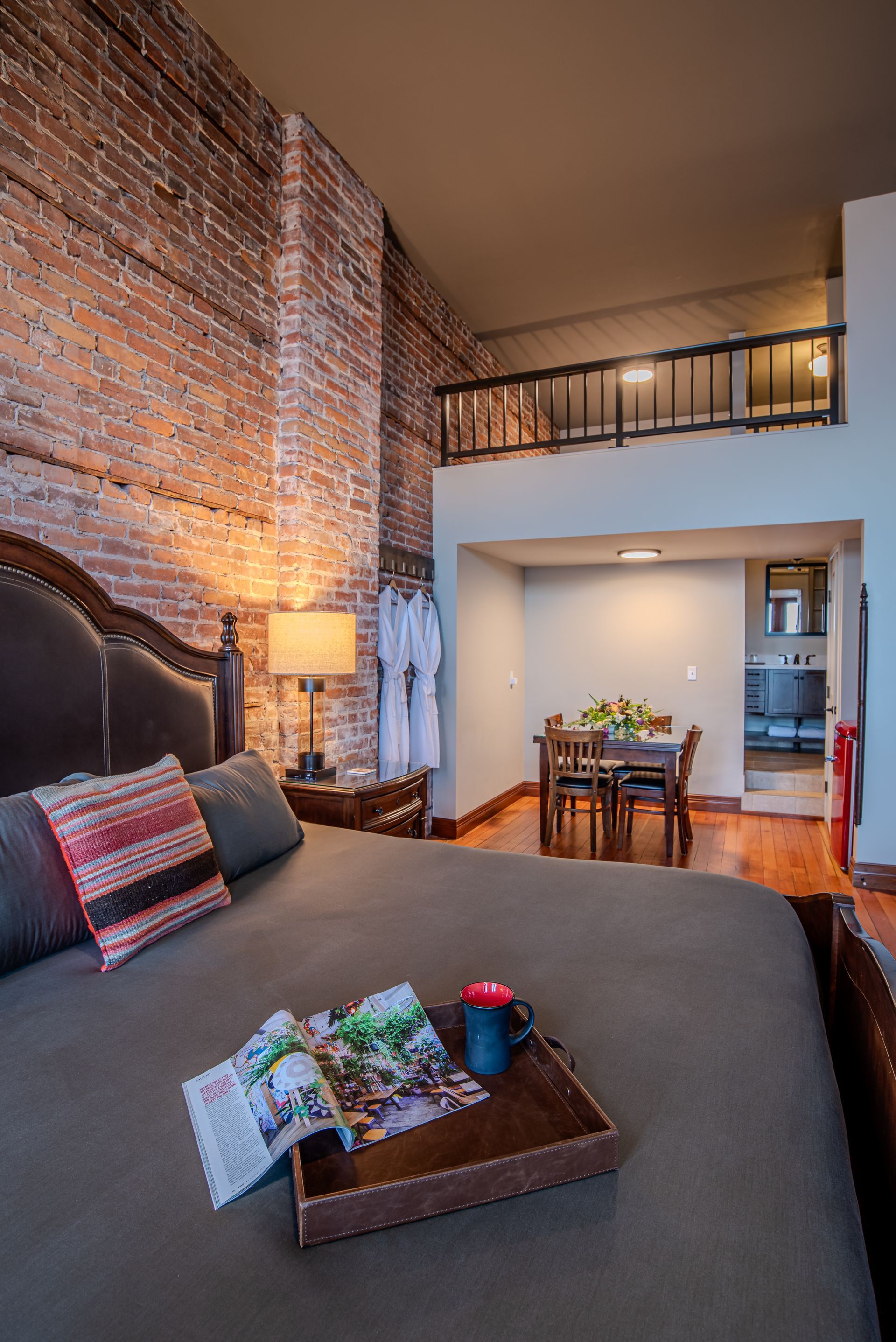 A bedroom with a brick wall and a tray of food on the bed.