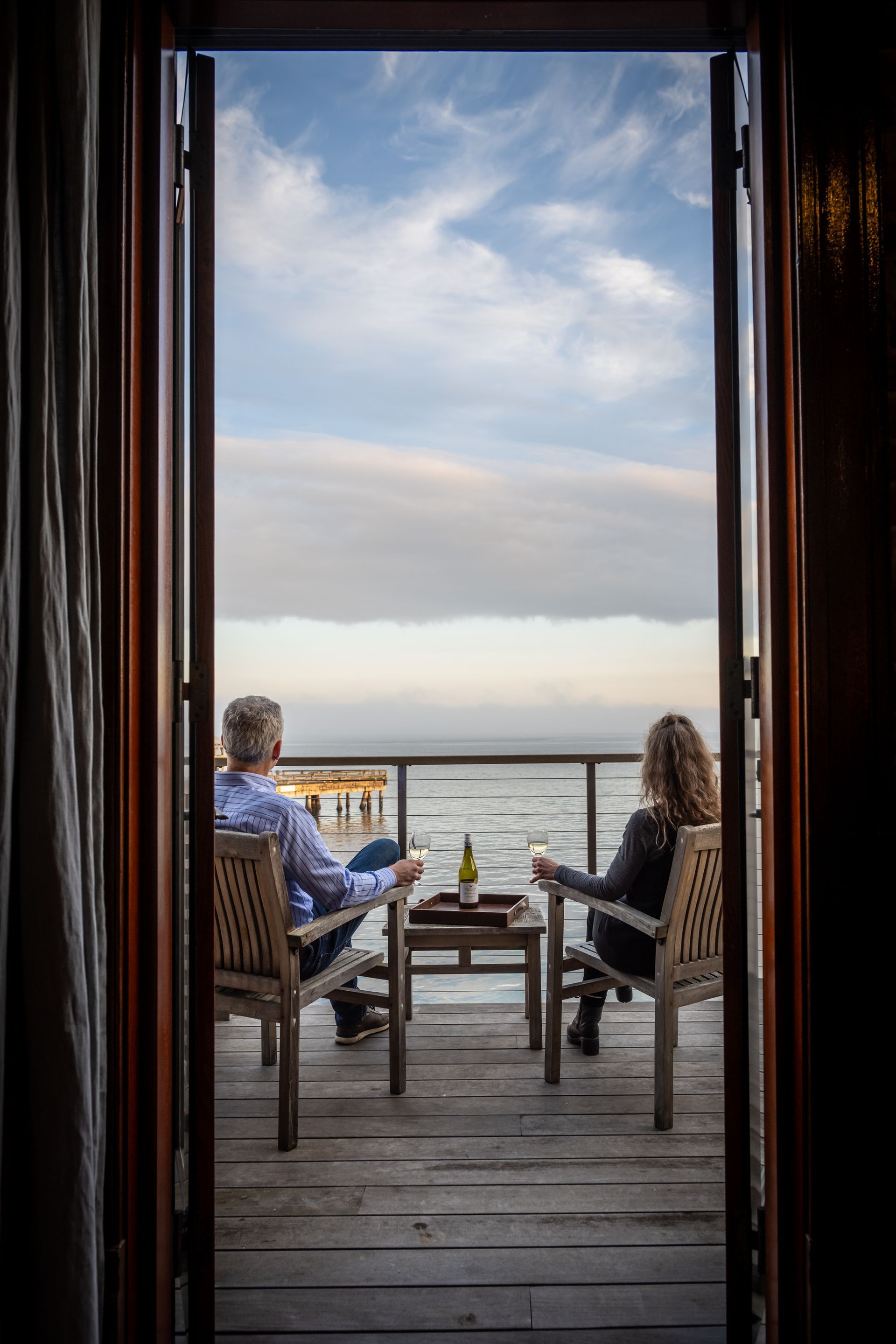A man and a woman are sitting on a balcony overlooking the ocean.