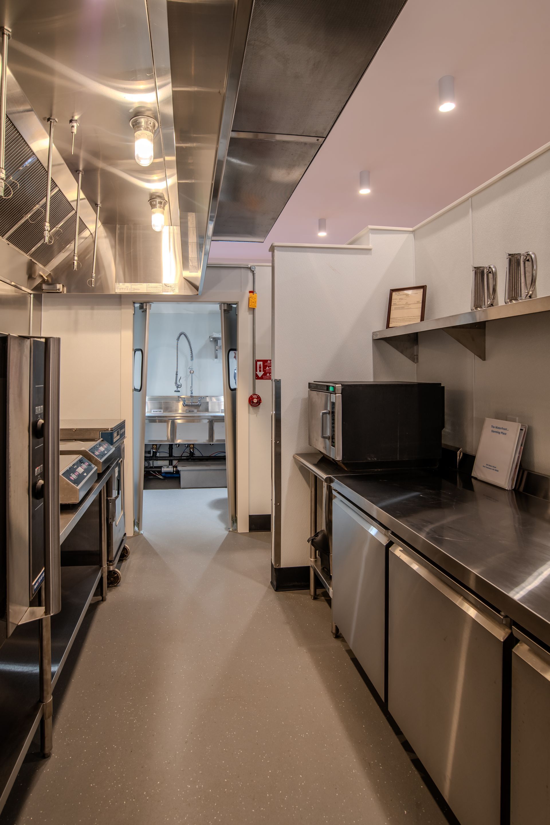A long kitchen with stainless steel appliances and a microwave. As an event space, The Waterfront at Sterming Place can accommodate up to 180 people for a stand-up reception and 100+ people seated at roundtables.