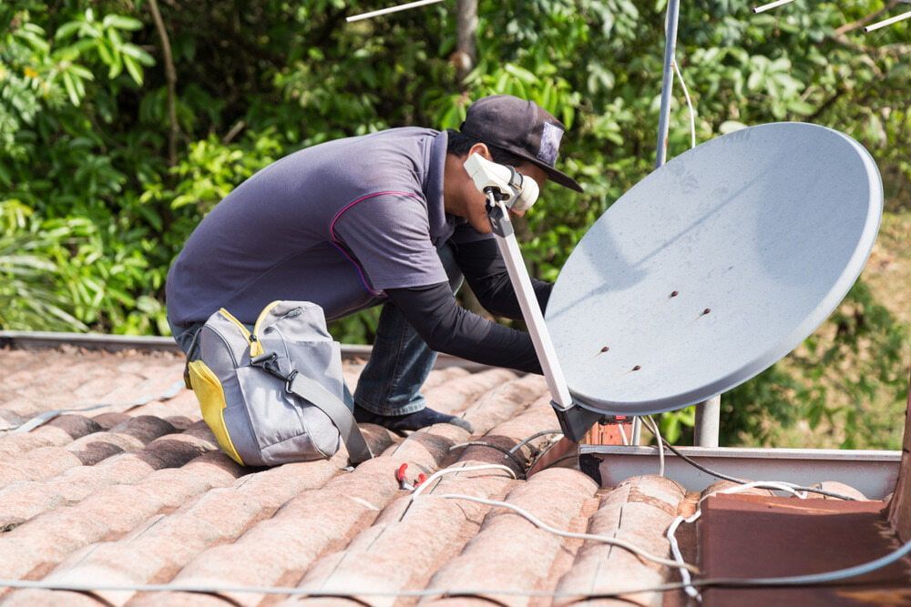 A Man Is Installing A Satellite Dish On The Roof Of A House — Homeland Electrical & Refrigeration In Braitling, NT