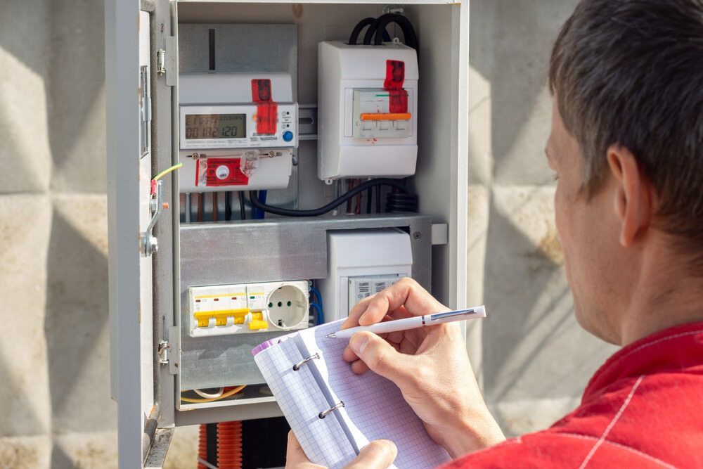 A Man Is Writing In A Notebook In Front Of An Electrical Box — Homeland Electrical & Refrigeration In Braitling, NT