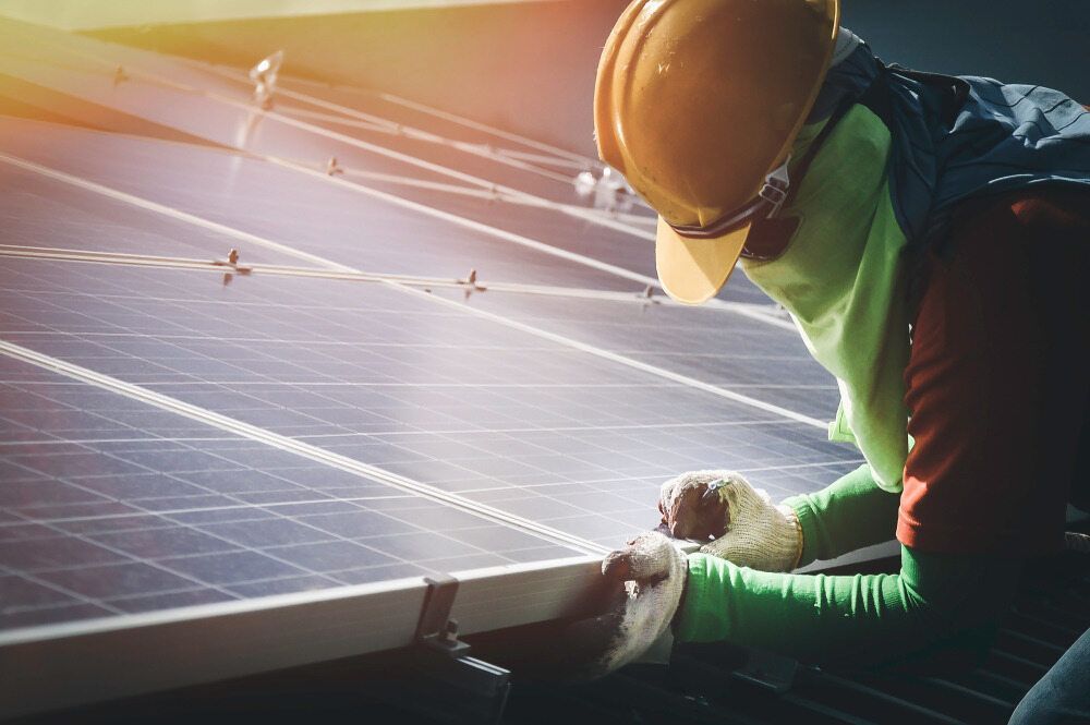 A Man Is Working On A Solar Panel On A Roof — Homeland Electrical & Refrigeration In Braitling, NT