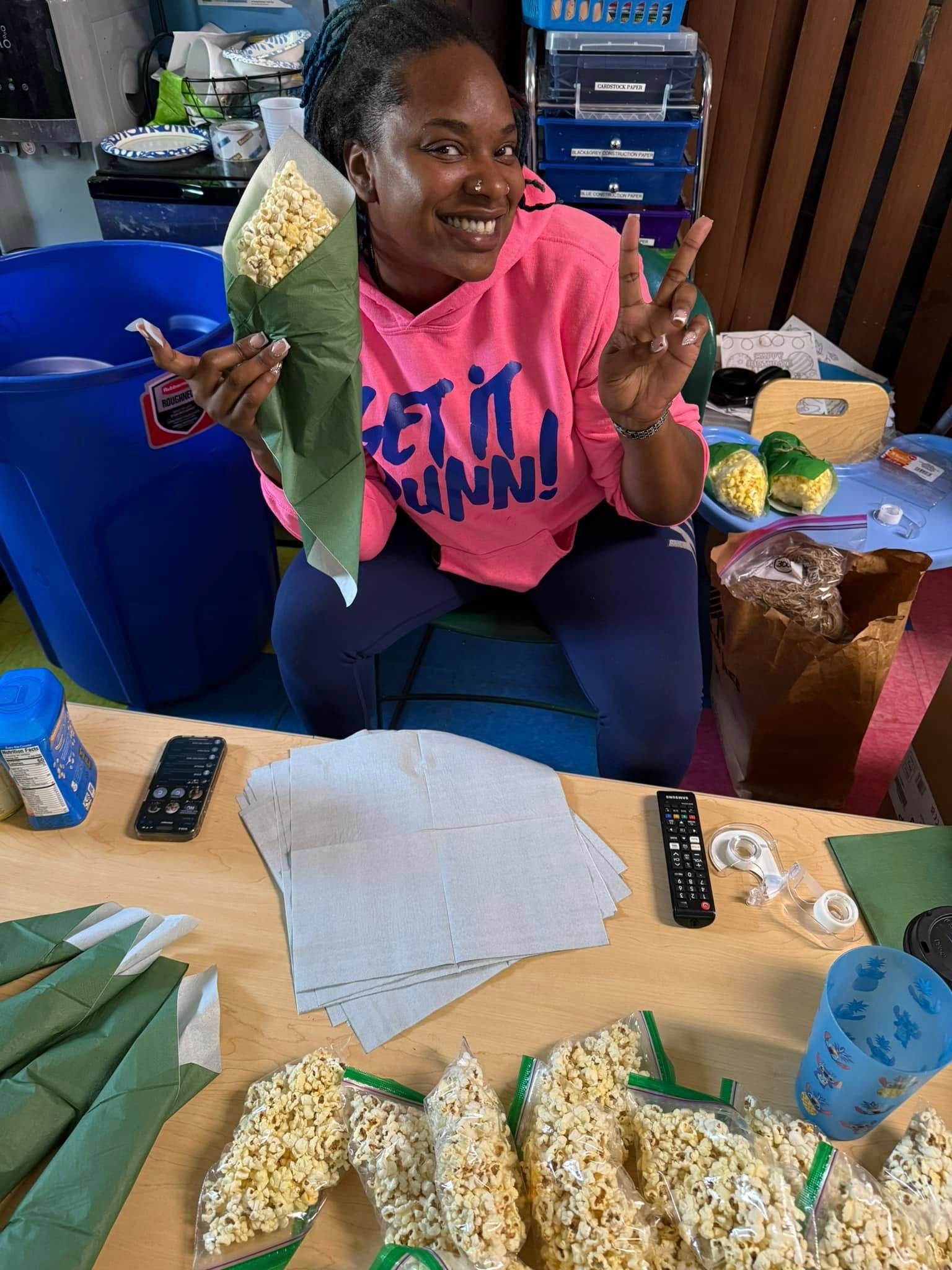 A woman is sitting at a table holding a bag of popcorn.