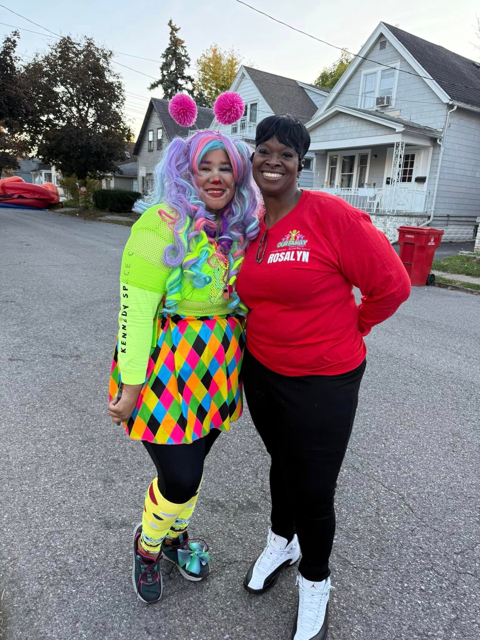 Two women in clown costumes are posing for a picture in front of a house.