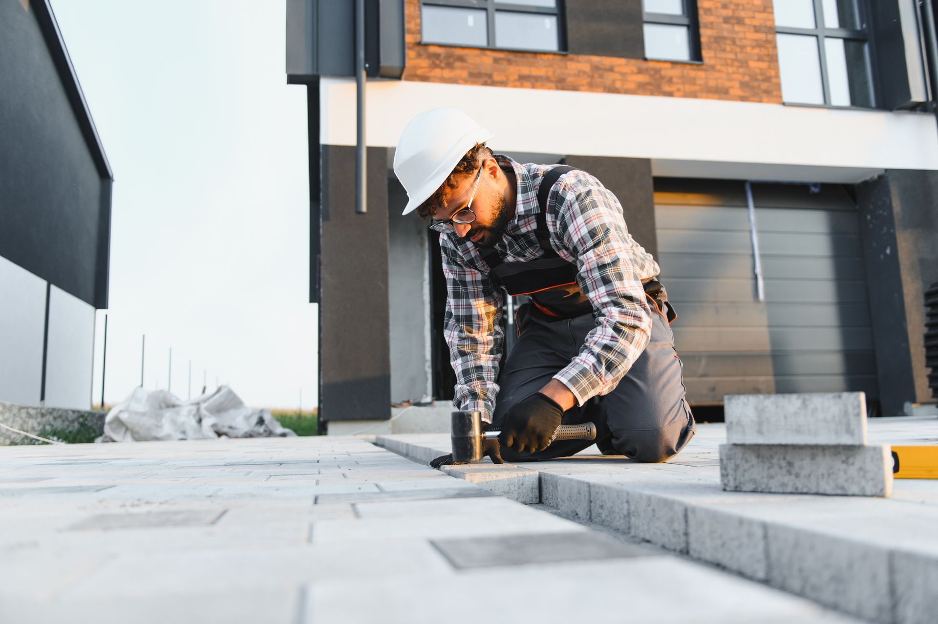 Paving contractor installing concrete pavers on residential driveway with safety gear.