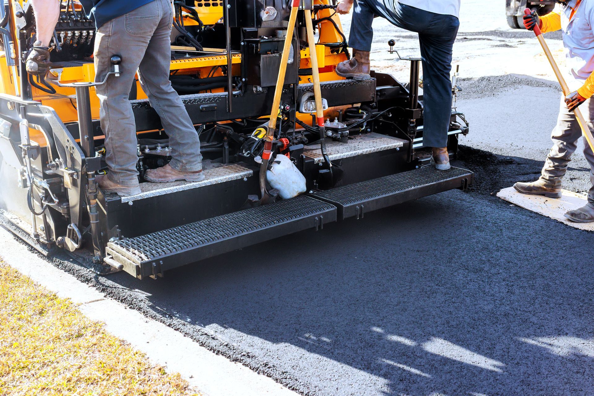Workers are using machinery to smoothly lay down fresh asphalt on street.