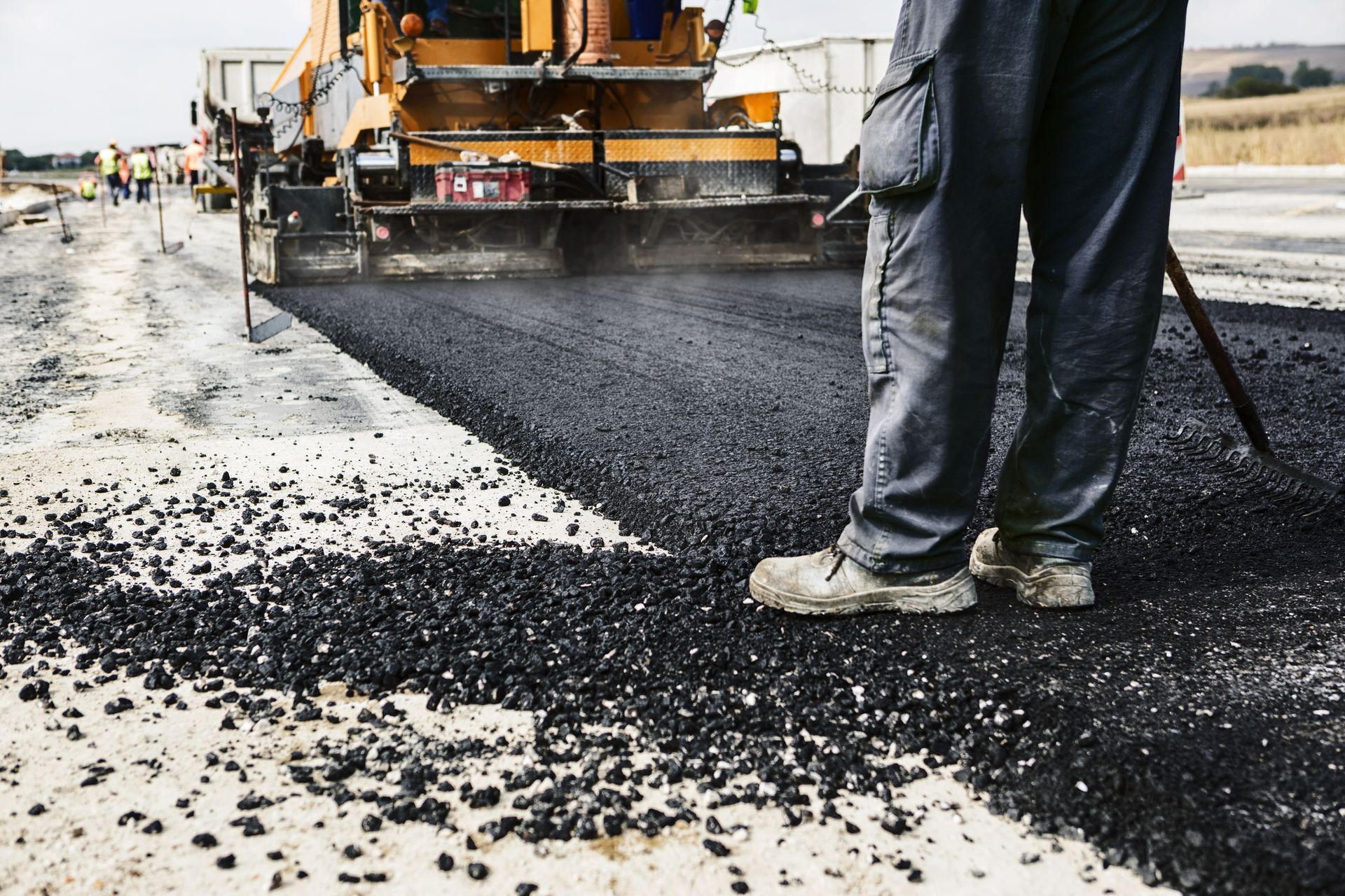 Worker standing near asphalt paving machine laying new road.