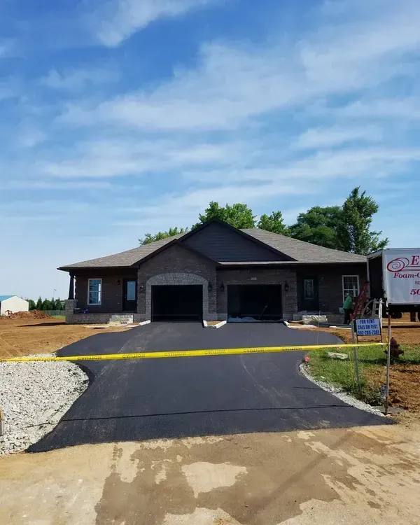 New brick duplex with two garages under a blue sky, construction in progress.