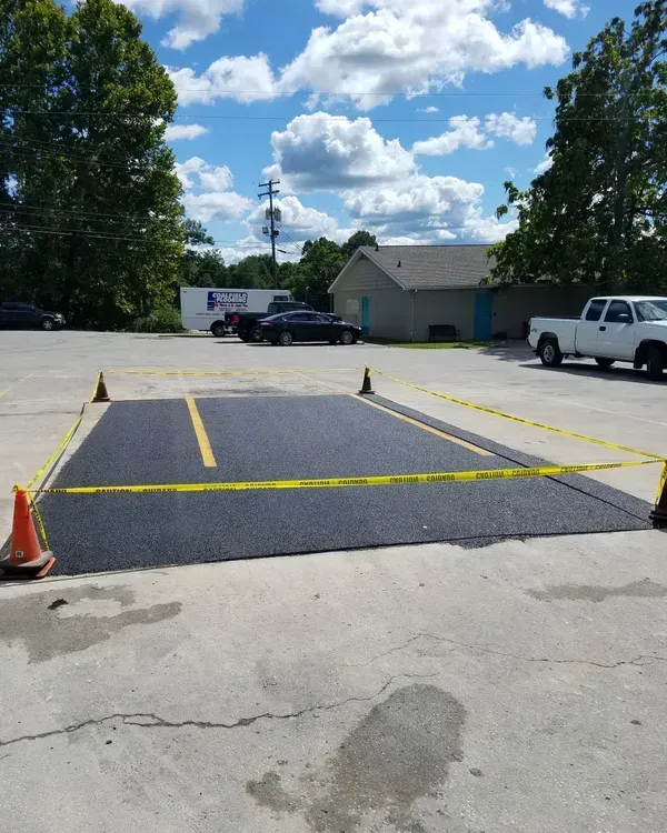 Freshly paved parking space with yellow tape and cones; outdoor daytime scene.