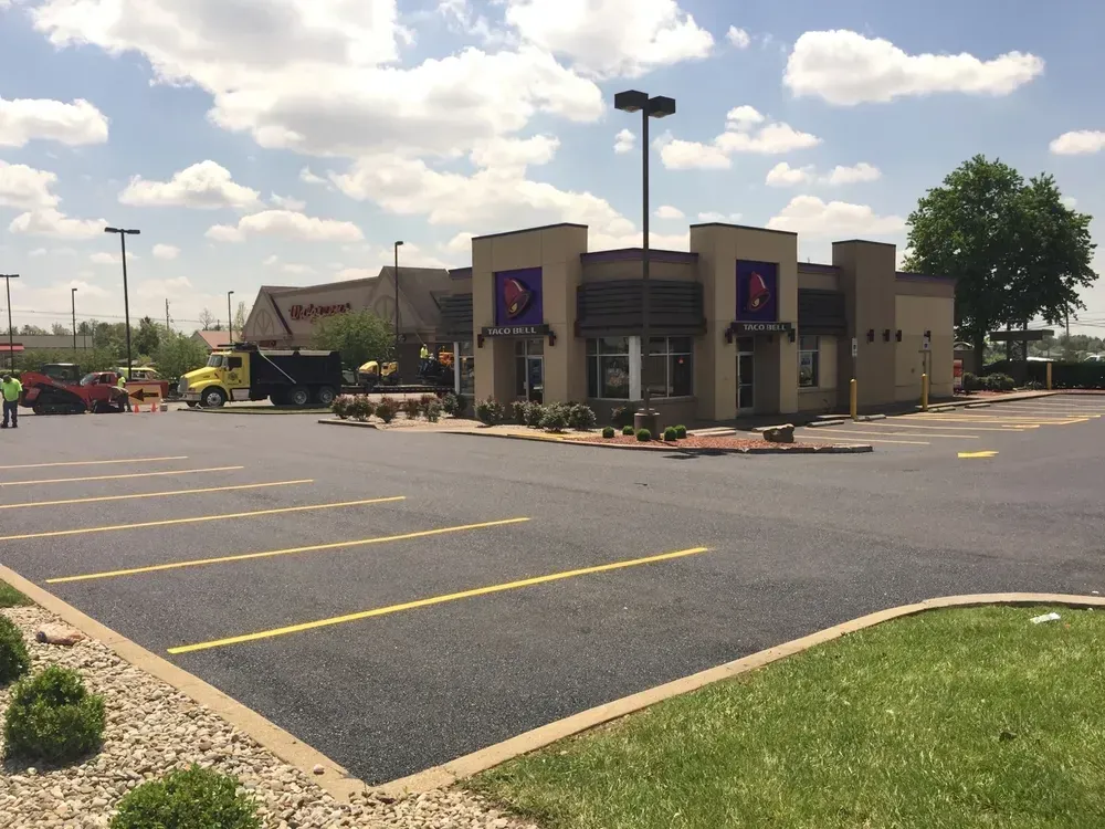 Newly paved Taco Bell parking lot on a sunny day. Building visible with landscaping.