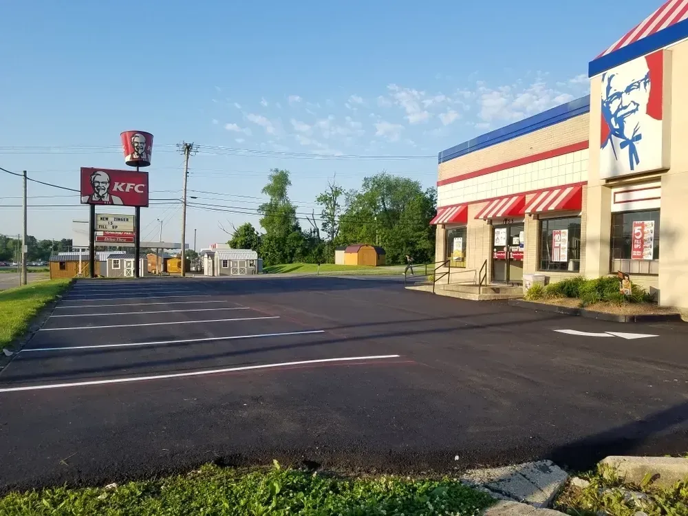KFC restaurant with a vacant parking lot on a sunny day. Large sign and building visible, red and white awnings.
