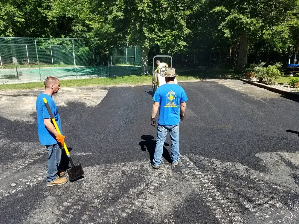Two men paving a parking lot; a roller compacts the asphalt.