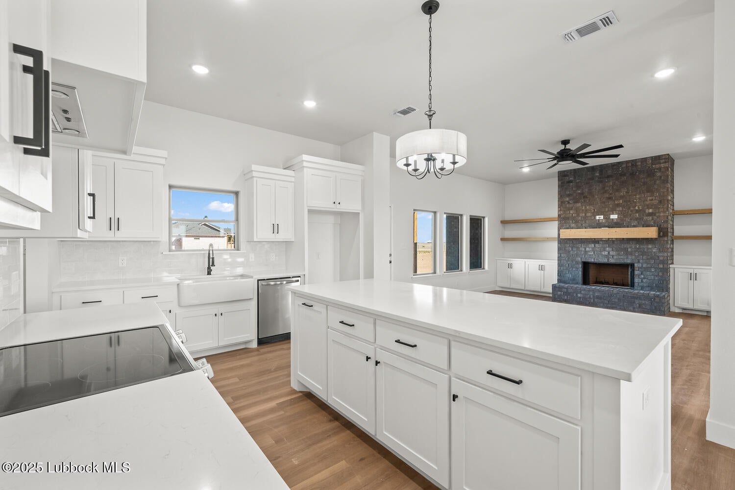 Bright, white kitchen with island, cabinetry, and cooktop. fireplpace, hardwood floors