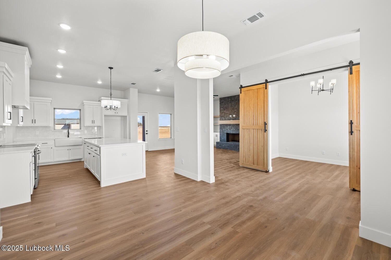 Bright open-plan kitchen and dining area with white cabinets, wood floors, and wooden sliding doors.