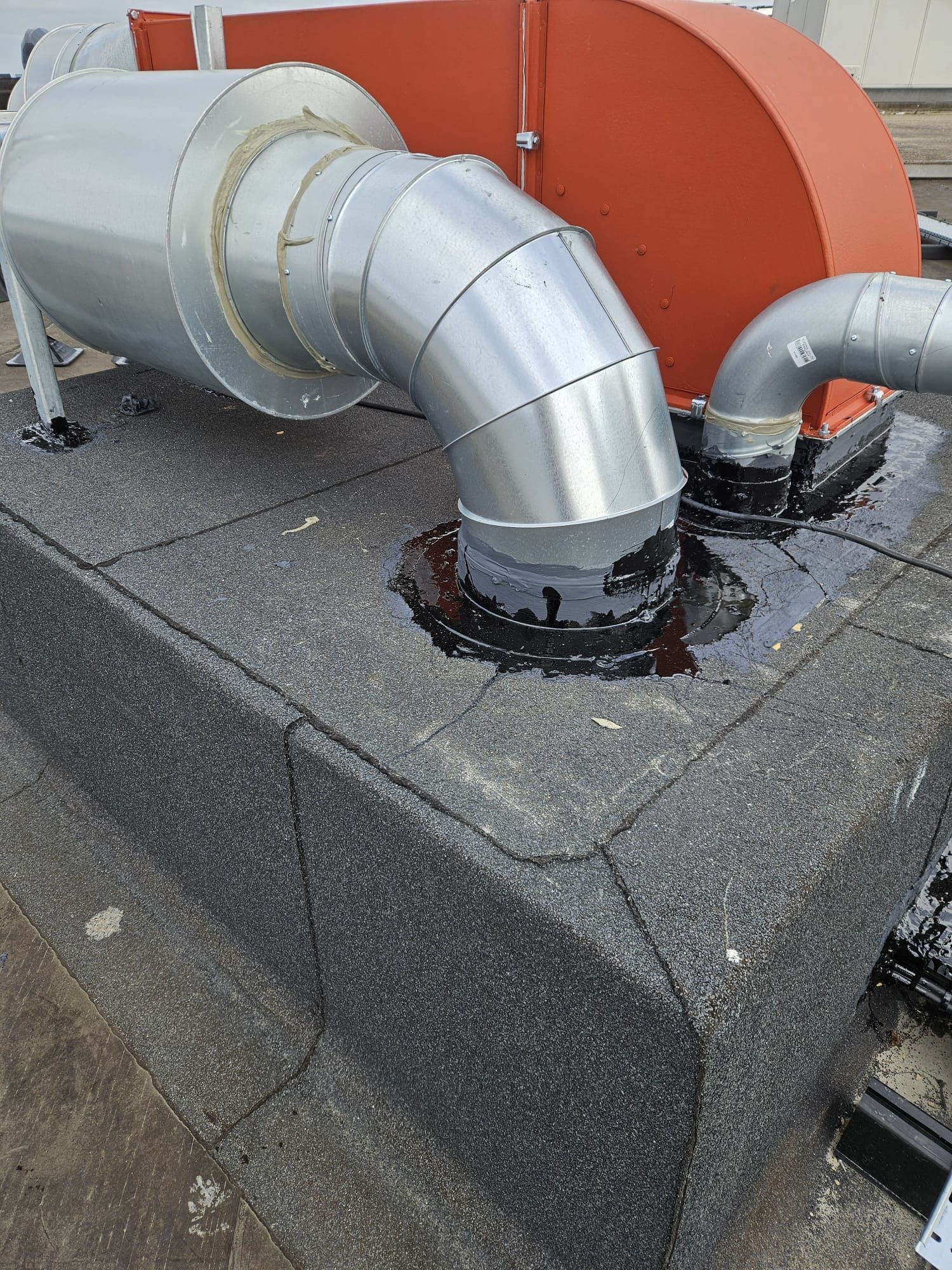 Rooftop ventilation system with silver pipes and orange casing, black tar sealant around pipe exits.