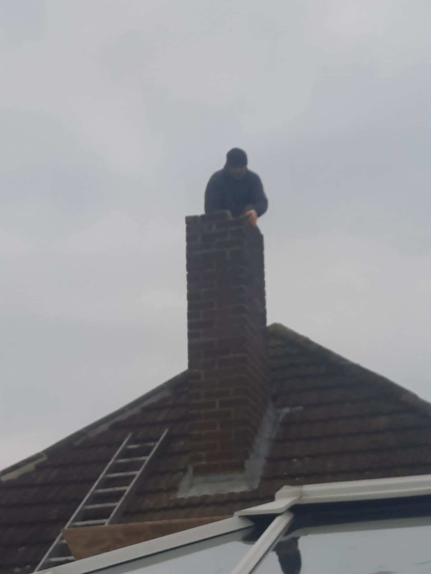 a man is sitting on top of a chimney on the roof of a house