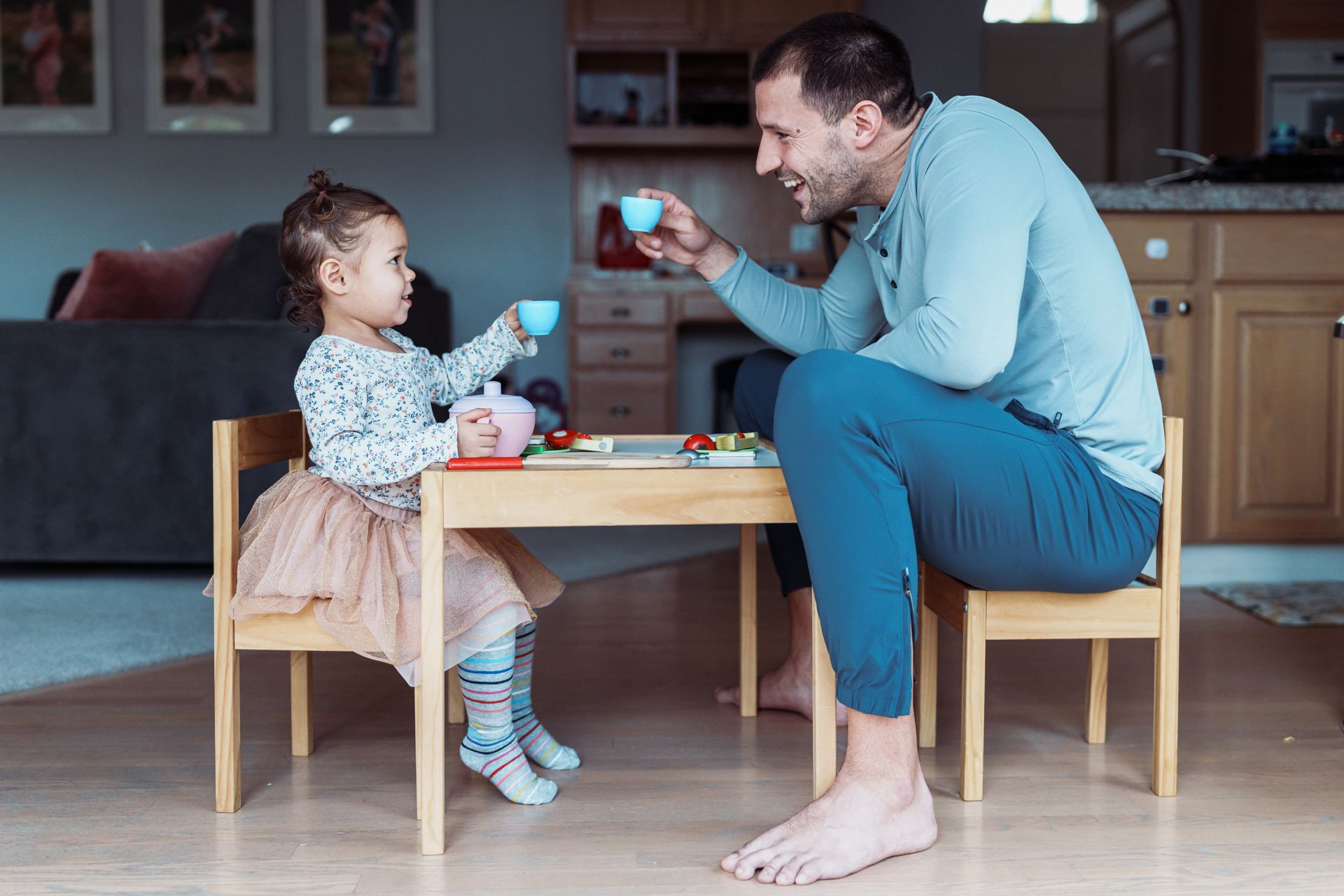 Man and child playing with toy tea set at small table in a home setting.