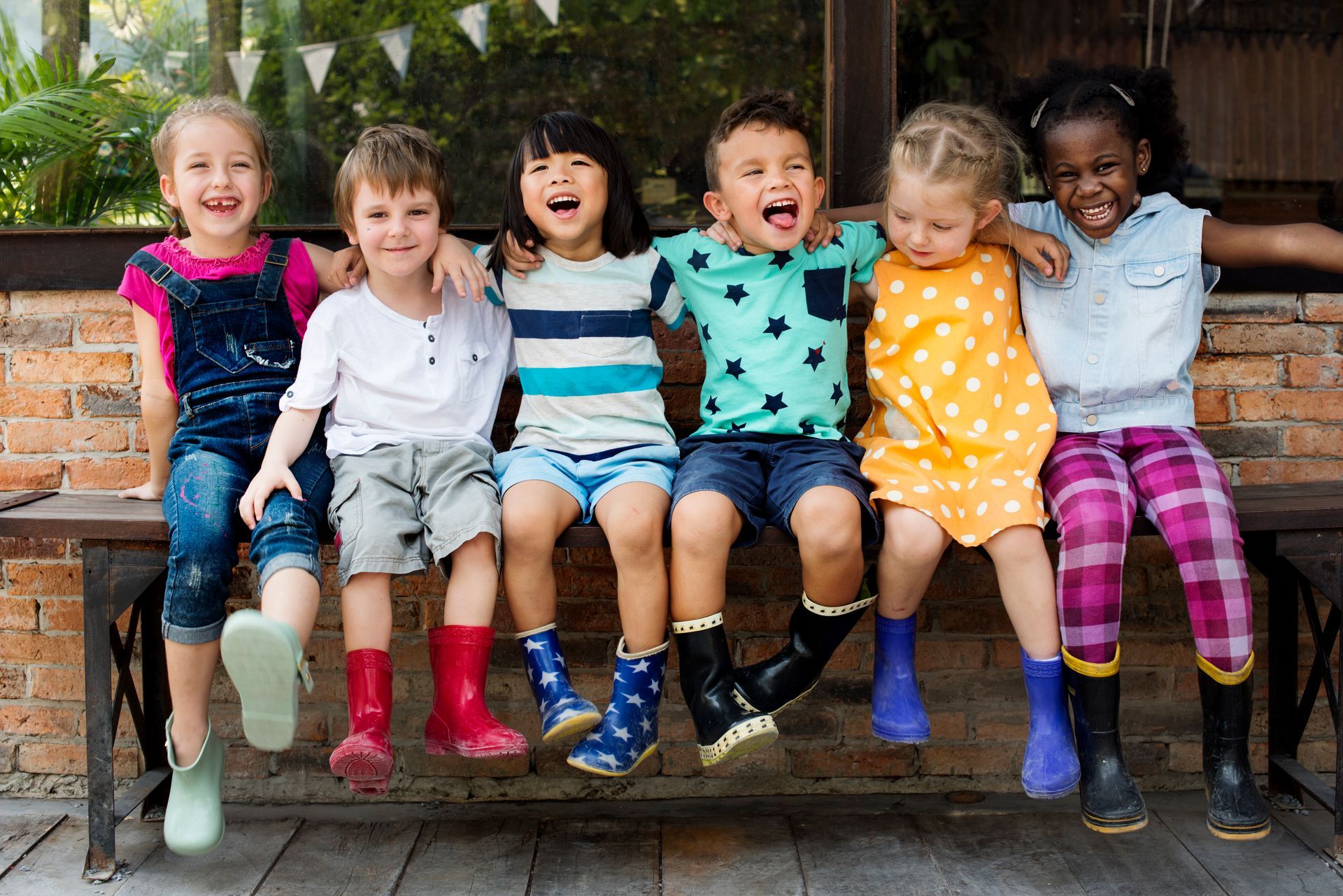 Group of children smiling and hugging, sitting on a wooden bench.