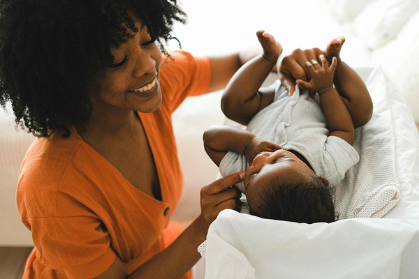 Woman in orange dress smiles at baby lying on changing pad.