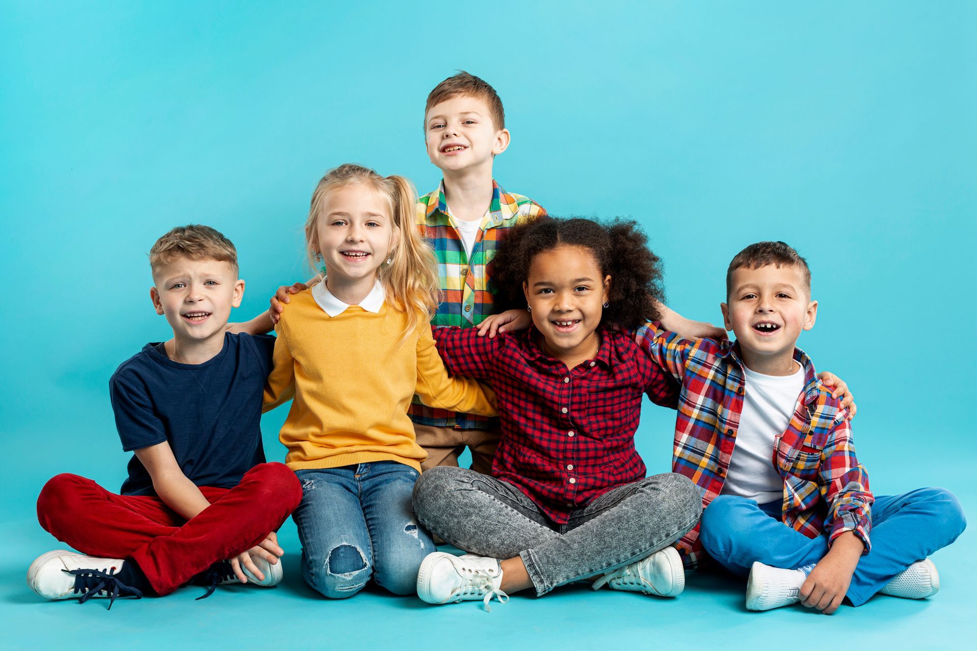 Group of children smiling and embracing, sitting against a blue background.