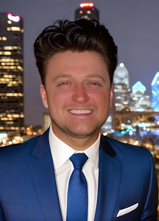A woman is sitting at a desk with a laptop and a vase of flowers.