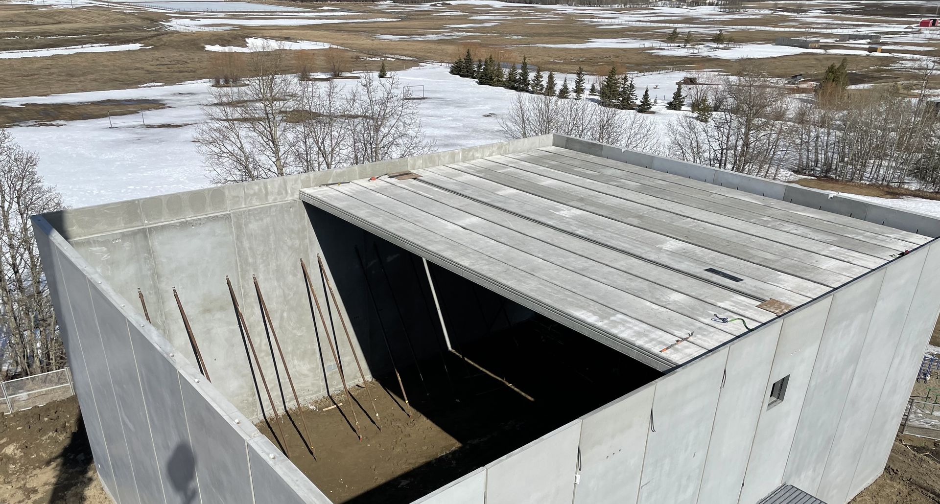 Concrete building under construction with precast roof slabs laid partially. Snowy field in the background.