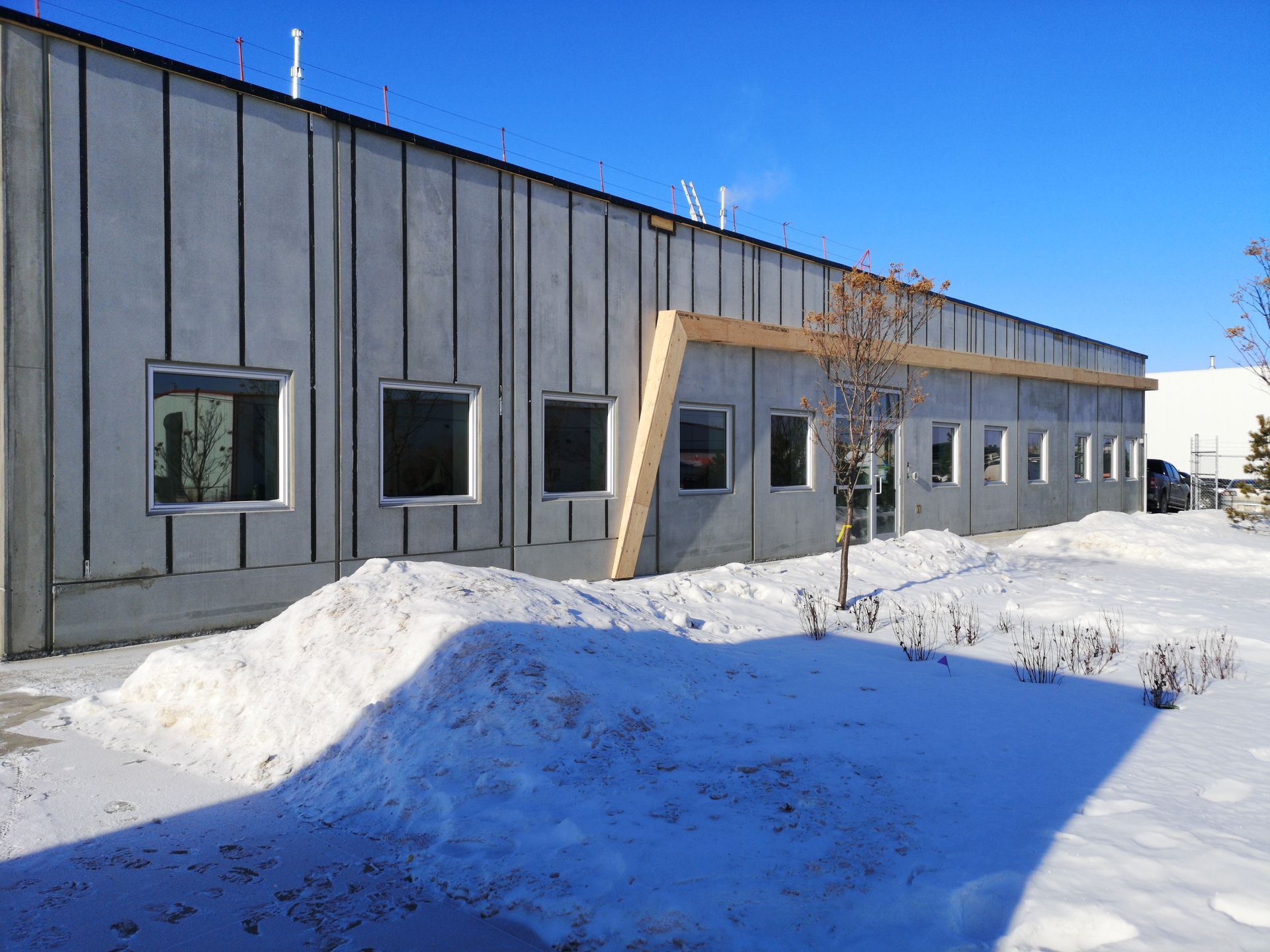 Exterior of a modern building with a gray facade and a row of windows, snow on the ground in front.