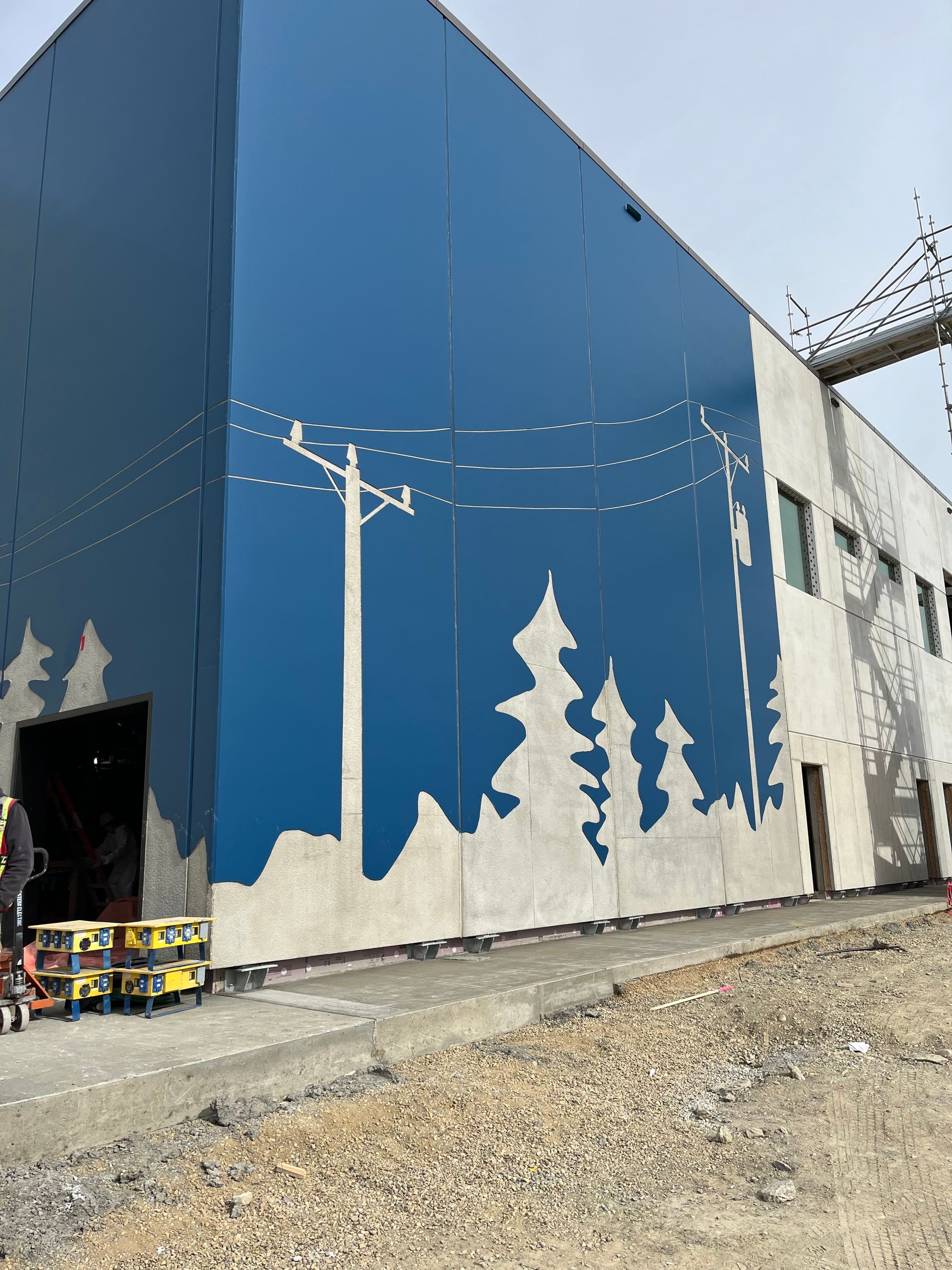 Blue and white mural on a building depicts a forest and telephone pole against a blue backdrop.