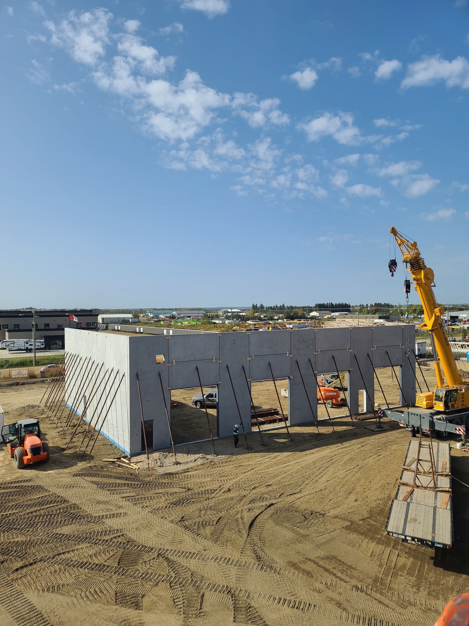Construction site with a partially built concrete structure, crane, and heavy machinery on a sunny day.