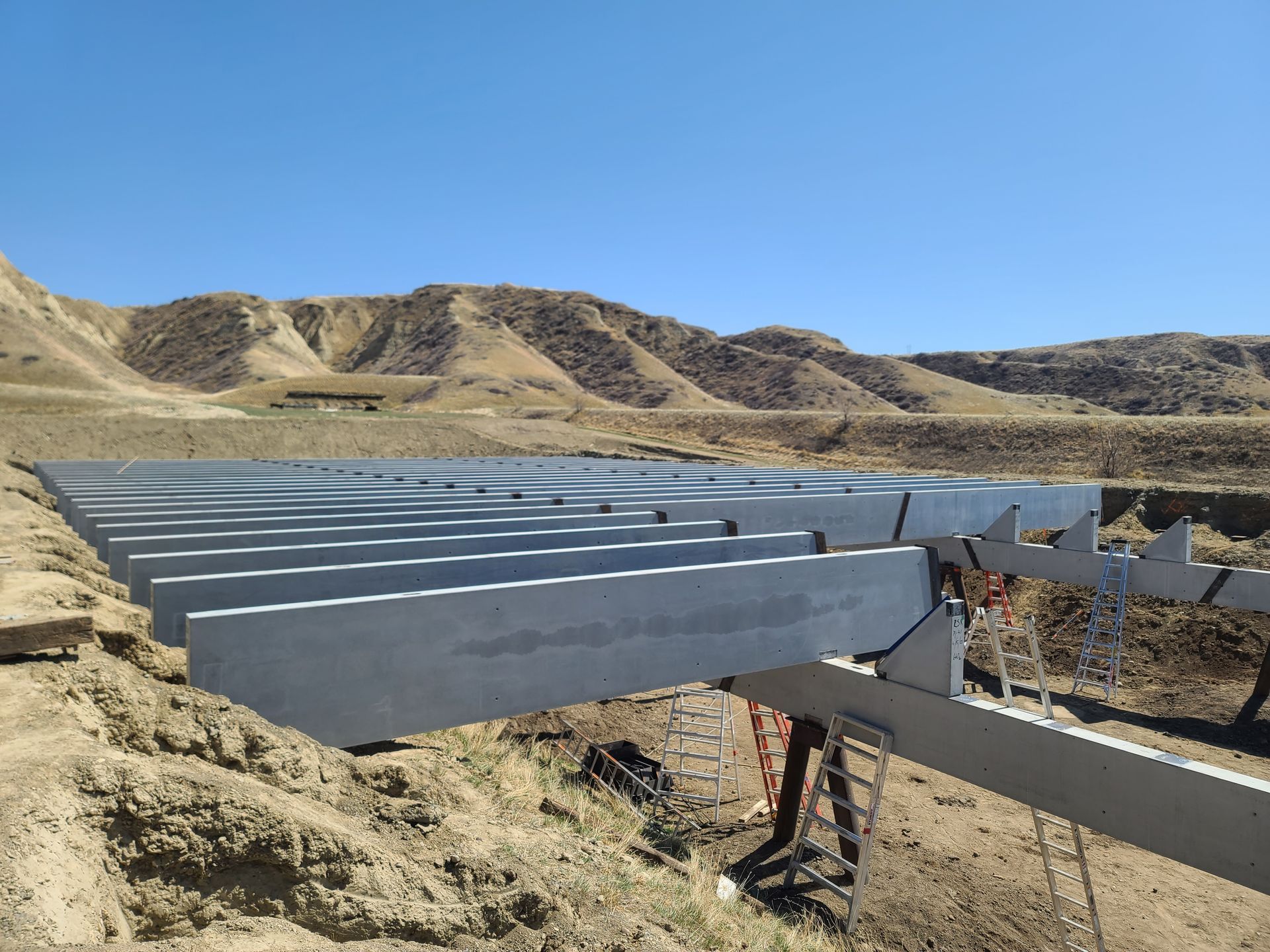 Construction of a solar panel array in a desert landscape. Gray support structures are in place, ready for panel installation, under a clear blue sky.