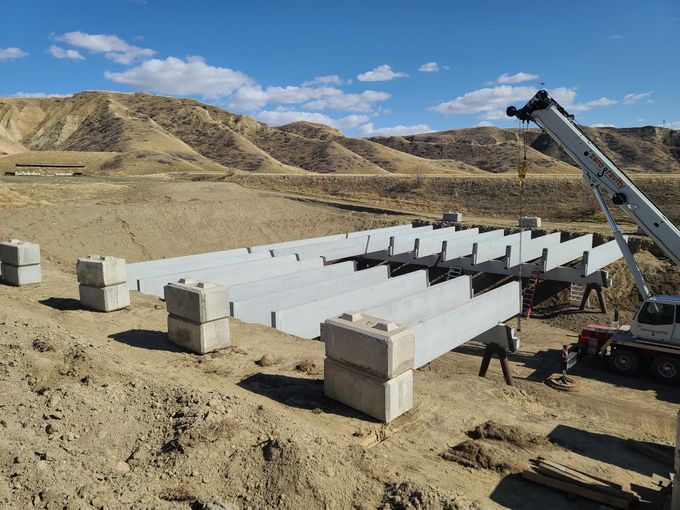 Construction site with concrete beams and blocks in a desert landscape, crane lifting beams into place.