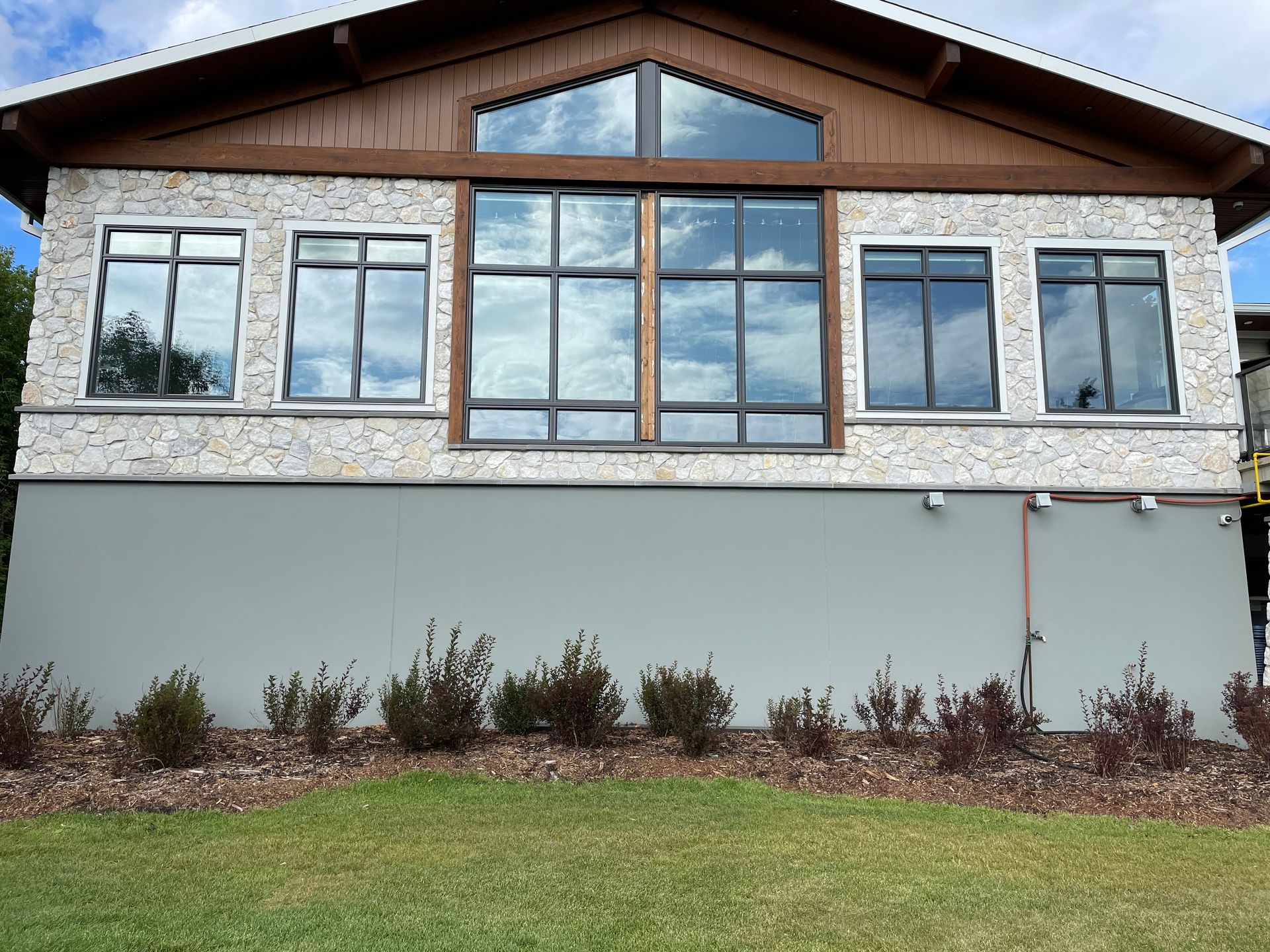 Building exterior with light-colored textured siding above a smooth gray lower wall. Several windows reflect the sky. Ground-level landscaping.