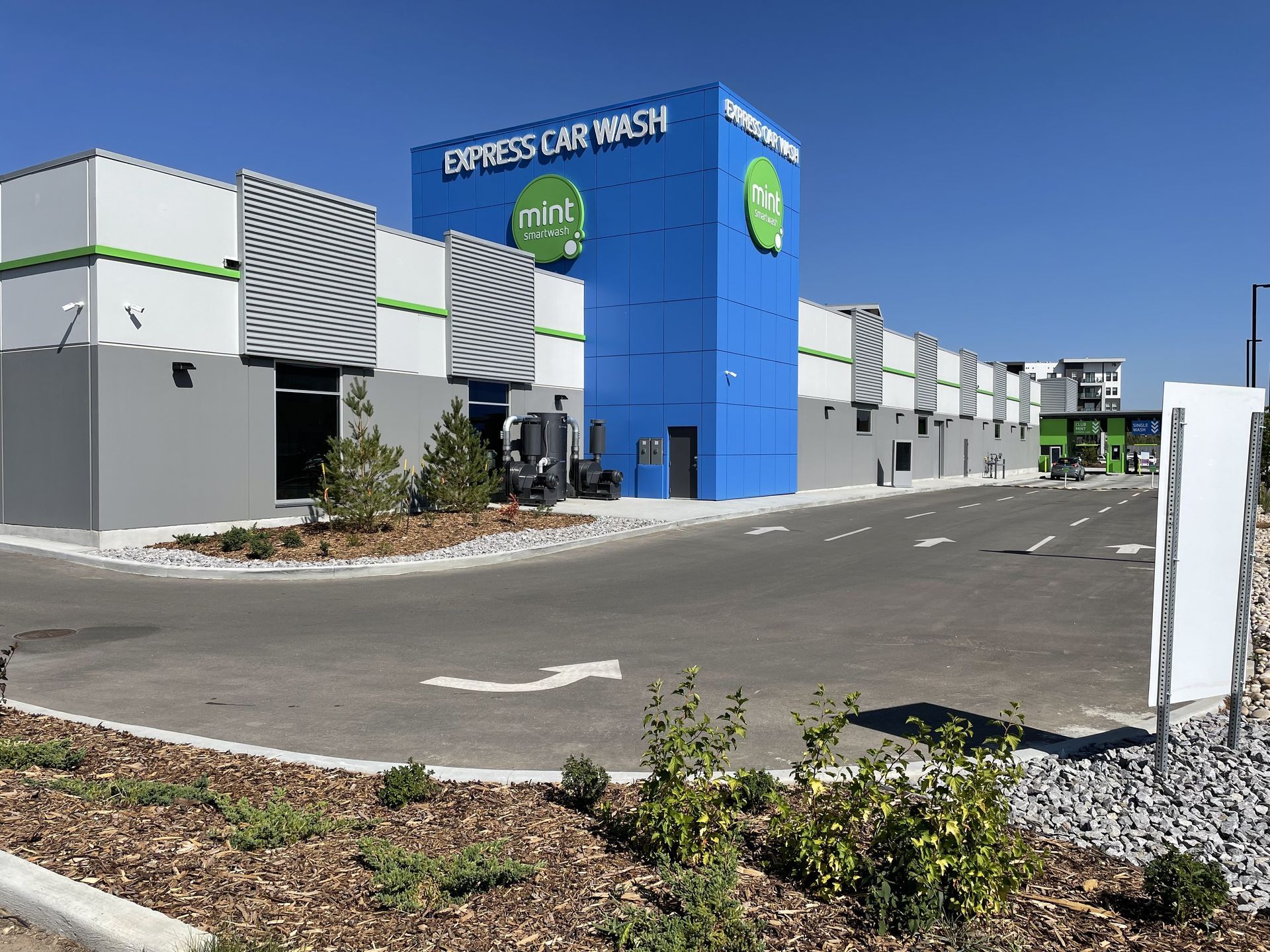Exterior view of a Mint Express Car Wash with a blue tower, grey and white building sections, and a paved drive.