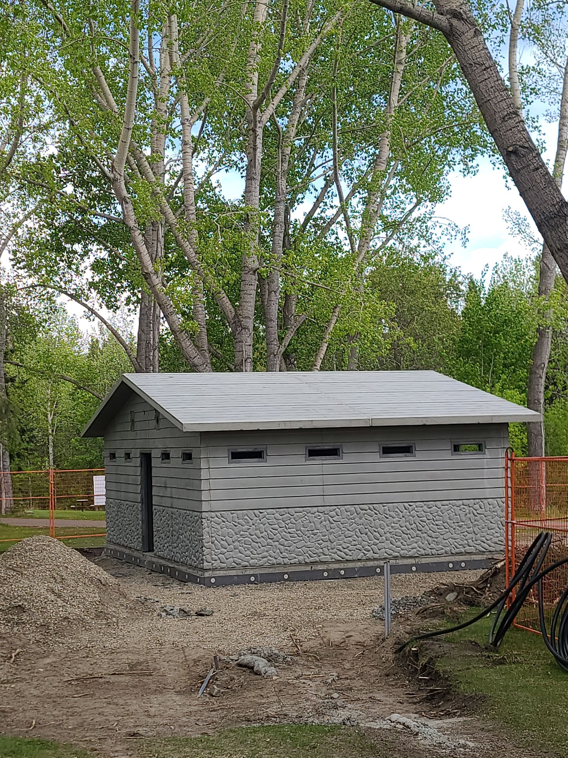 Stone building with a gray roof, likely a public restroom. Trees form a backdrop.