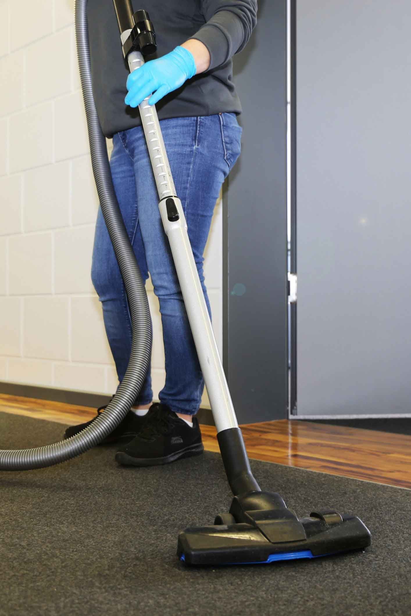 A person wearing blue gloves is using a vacuum cleaner on a carpet.