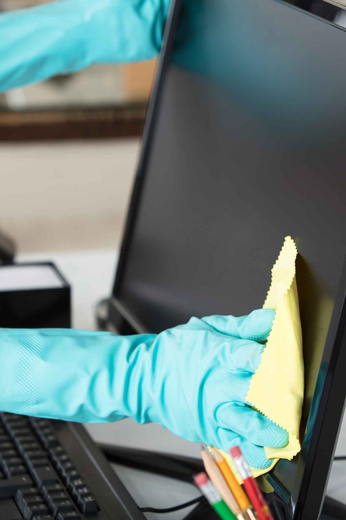 A person wearing blue gloves is cleaning a computer screen with a cloth.