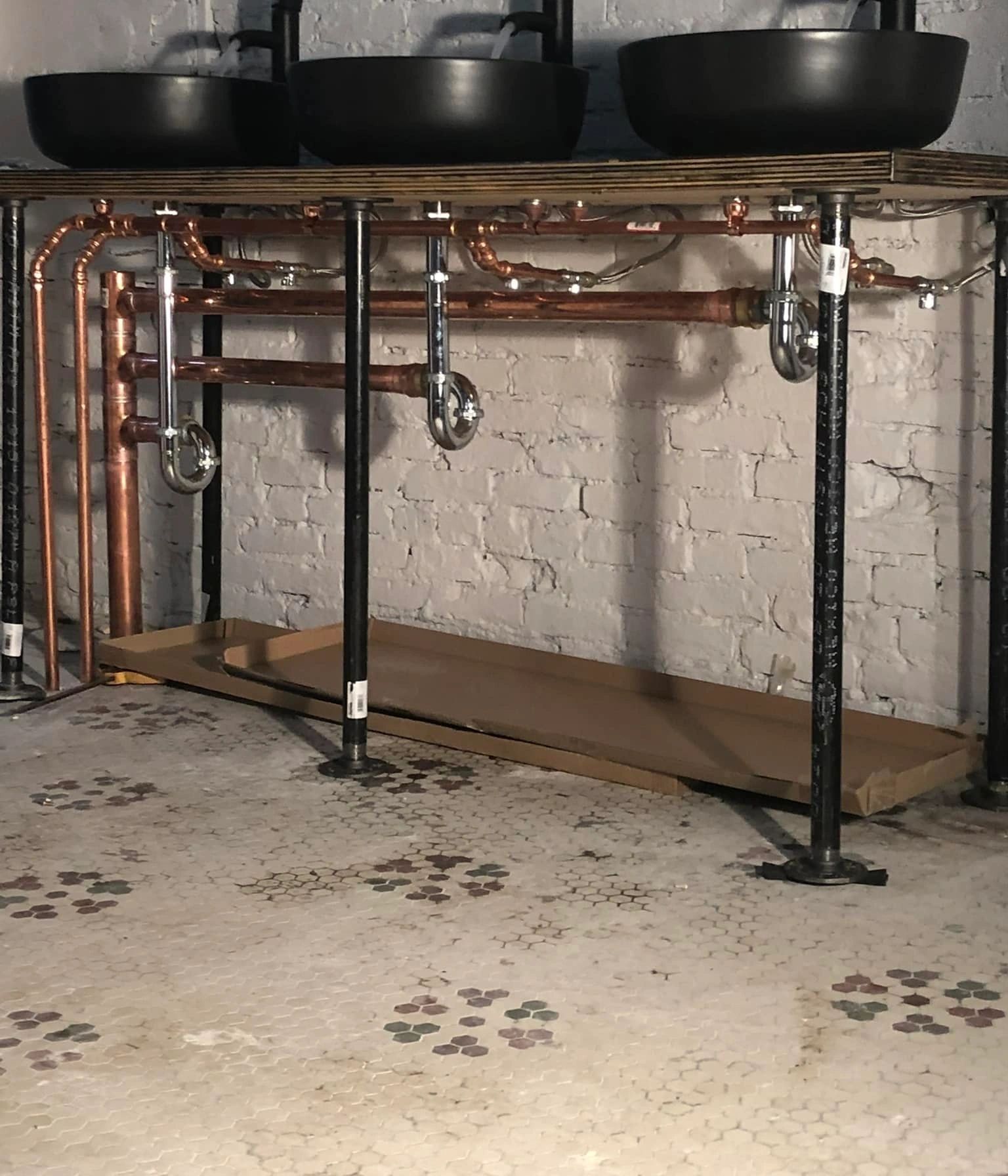 Two black sinks are under a wooden table with copper pipes