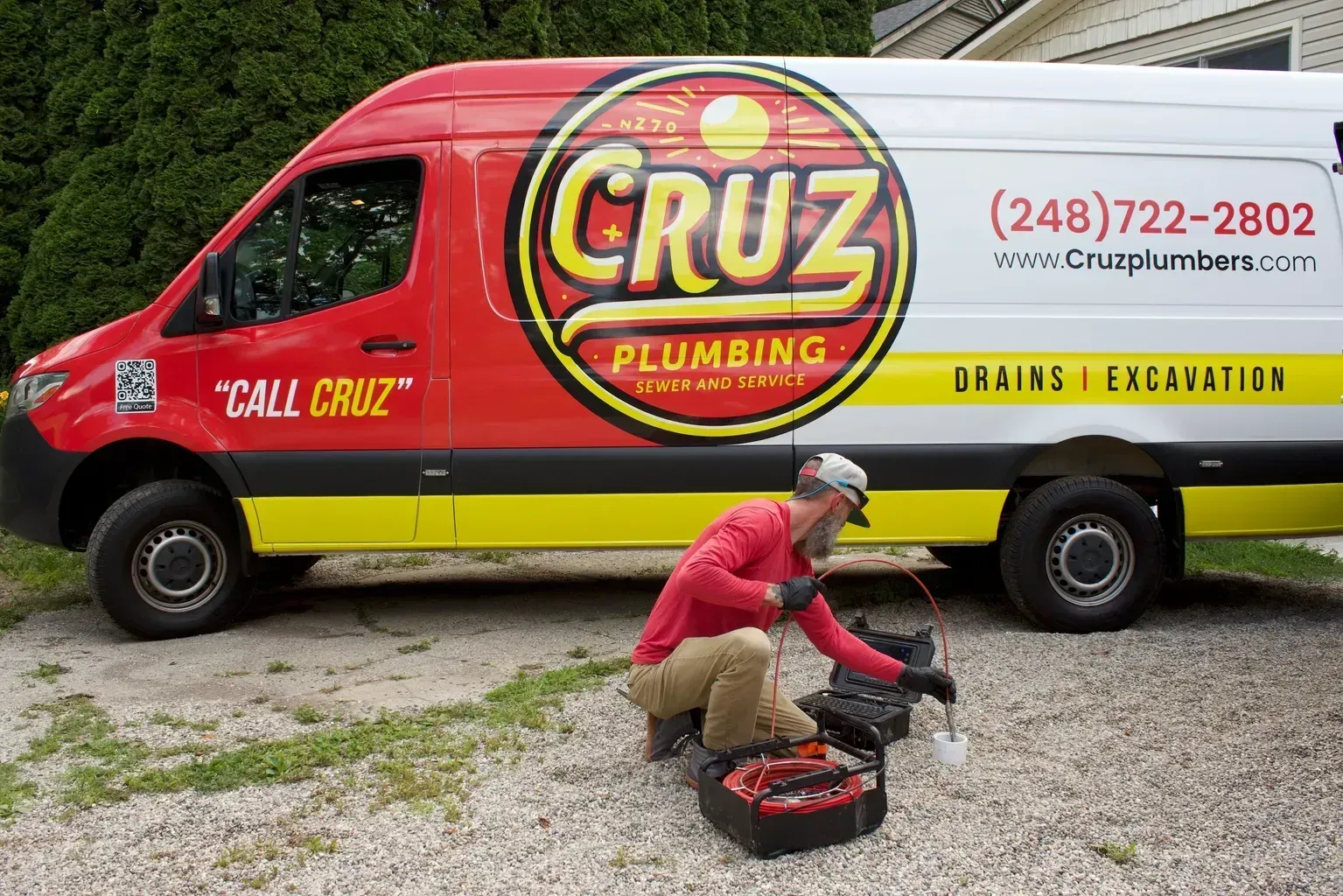 A man is kneeling in front of a cruz plumbing van.